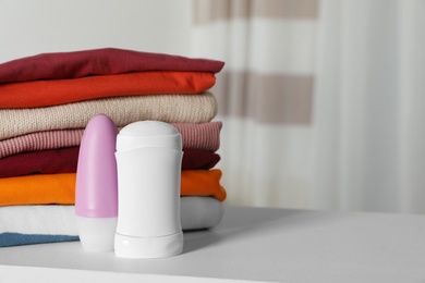 Photo of Deodorants near stack of clean clothes on white table. Space for text