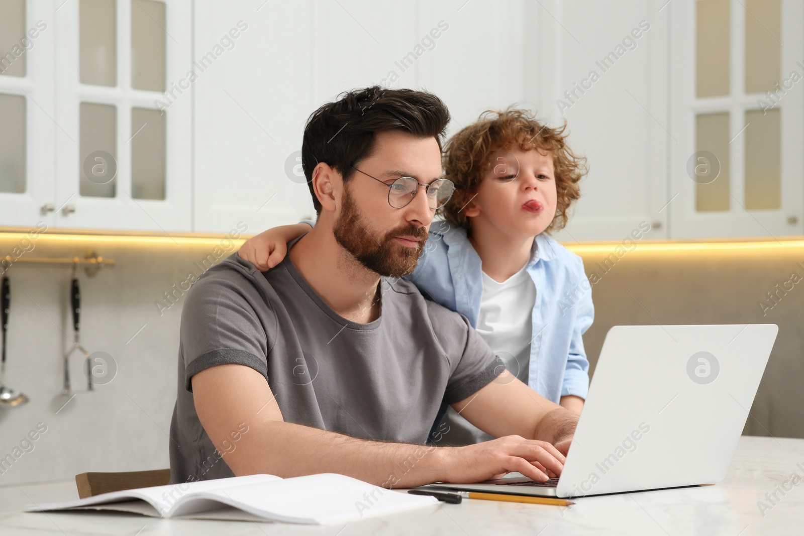 Photo of Man with laptop working remotely at home. Father and son at desk