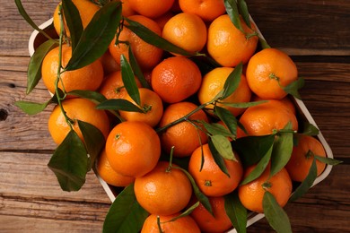 Fresh tangerines with green leaves in crate on wooden table, top view