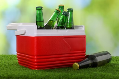 Photo of Plastic cool box with glasses of drink on artificial grass, closeup