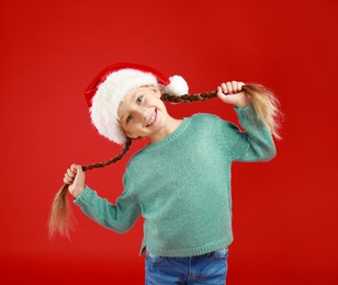 Image of Happy little child in Santa hat on red background. Christmas celebration