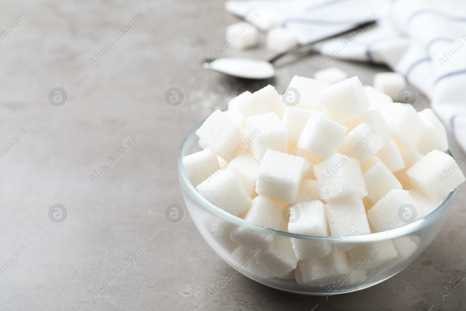 Photo of Refined sugar cubes in glass bowl on grey table. Space for text