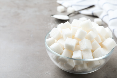 Refined sugar cubes in glass bowl on grey table. Space for text