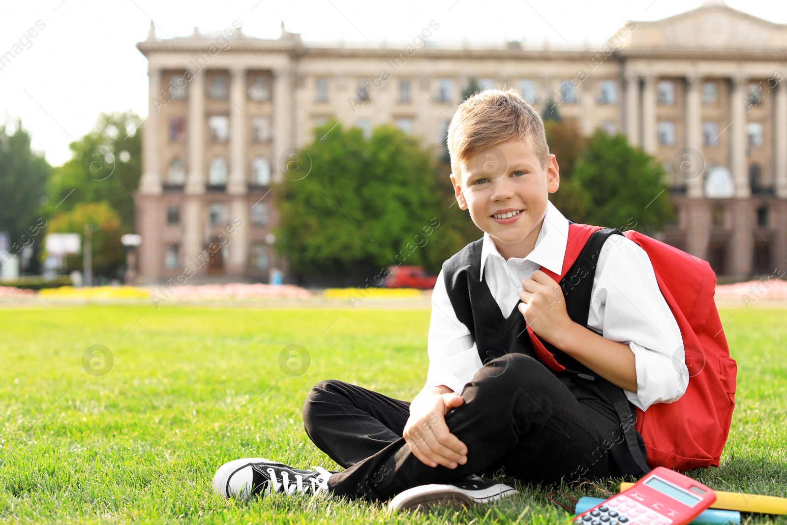 Photo of Schoolboy with stationery sitting on grass outdoors