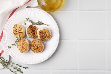 Heads of fried garlic with thyme and oil on white table, flat lay. Space for text