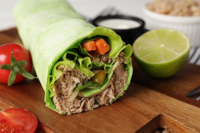 Photo of Delicious tortilla wrap with tuna on wooden board, closeup