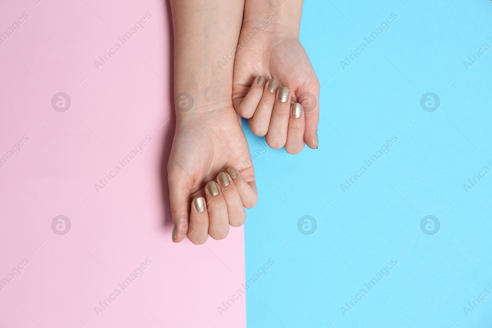 Photo of Woman with golden manicure on color background, top view. Nail polish trends