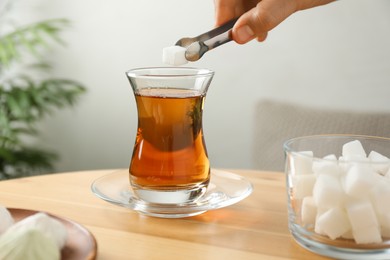 Woman adding sugar cube into aromatic tea at wooden table indoors, closeup