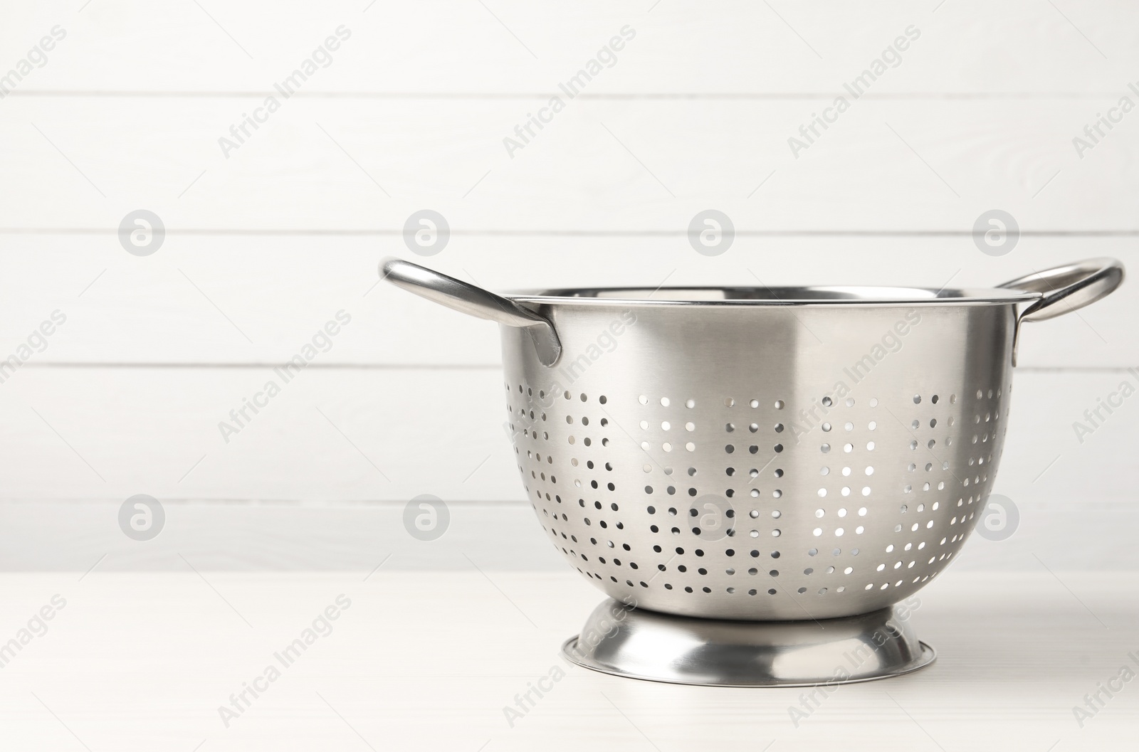 Photo of Metal colander on white wooden table. Space for text