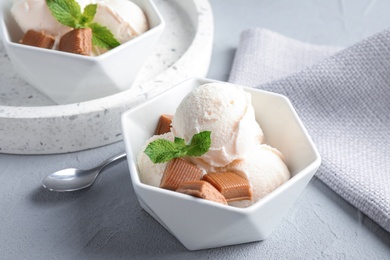 Photo of Bowl of ice cream with caramel candies and mint on light grey table