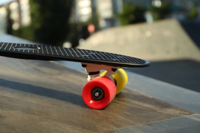 Photo of Modern black skateboard with colorful wheels on ramp outdoors, closeup