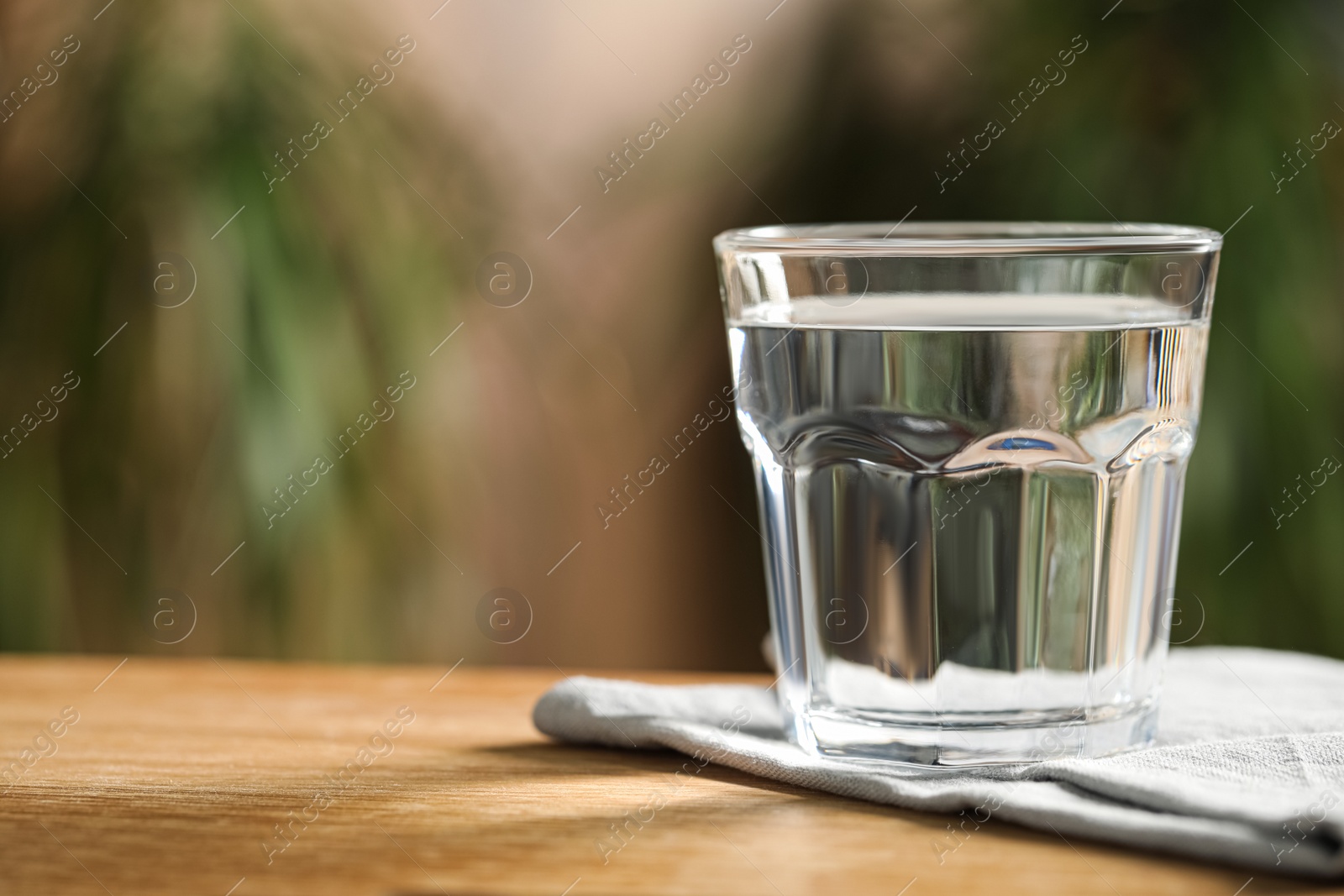 Photo of Glass of pure water on wooden table against blurred background, space for text