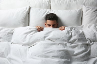 Handsome man sleeping under soft blanket in bed at home