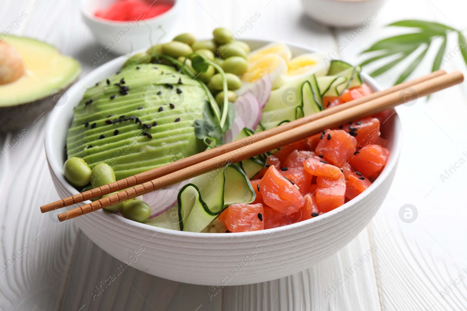 Photo of Delicious poke bowl with avocado, fish and edamame beans on white wooden table, closeup