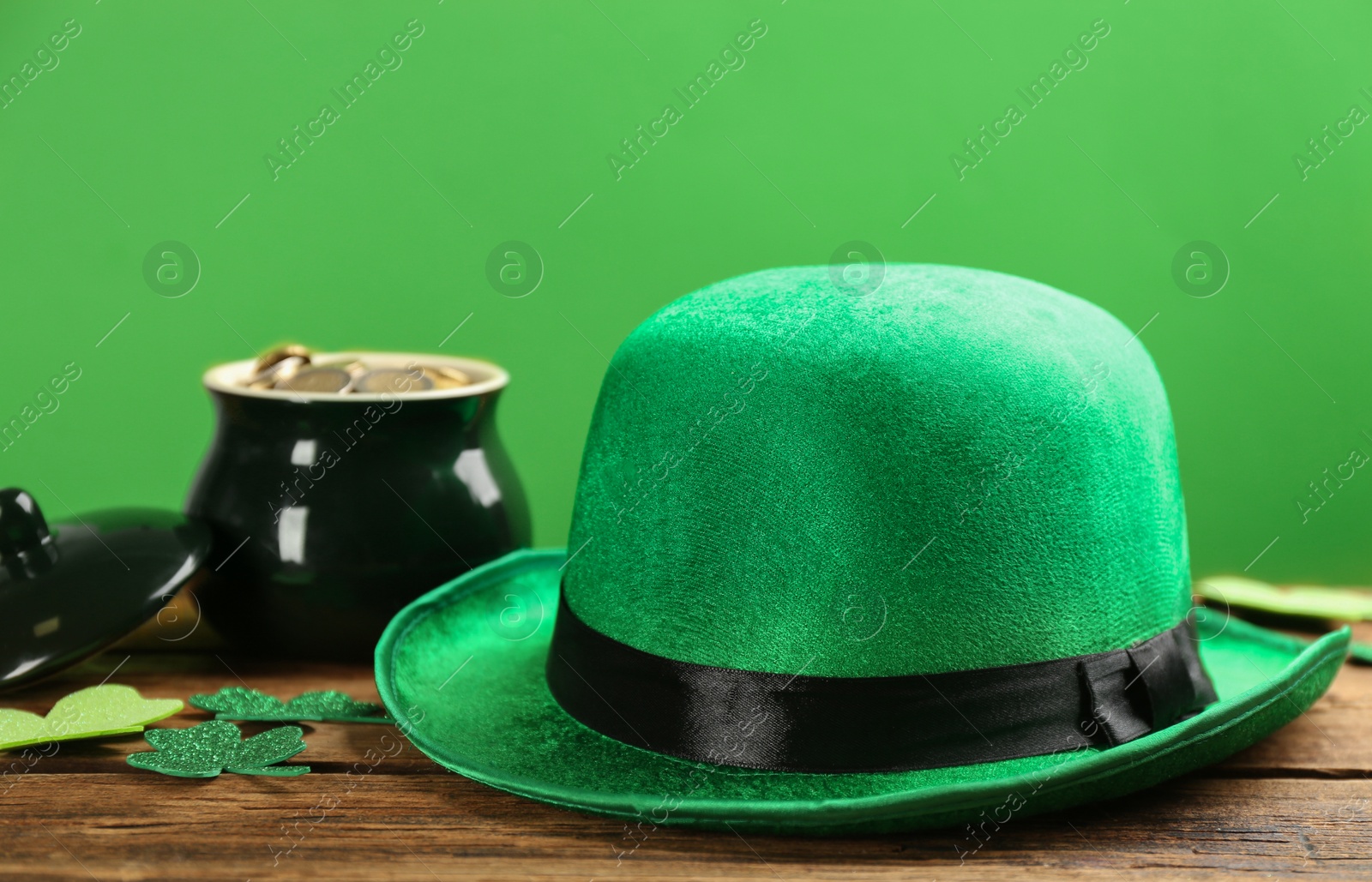 Photo of Leprechaun hat, decorative clover leaves and pot of gold on wooden table against green background. St Patrick's Day celebration