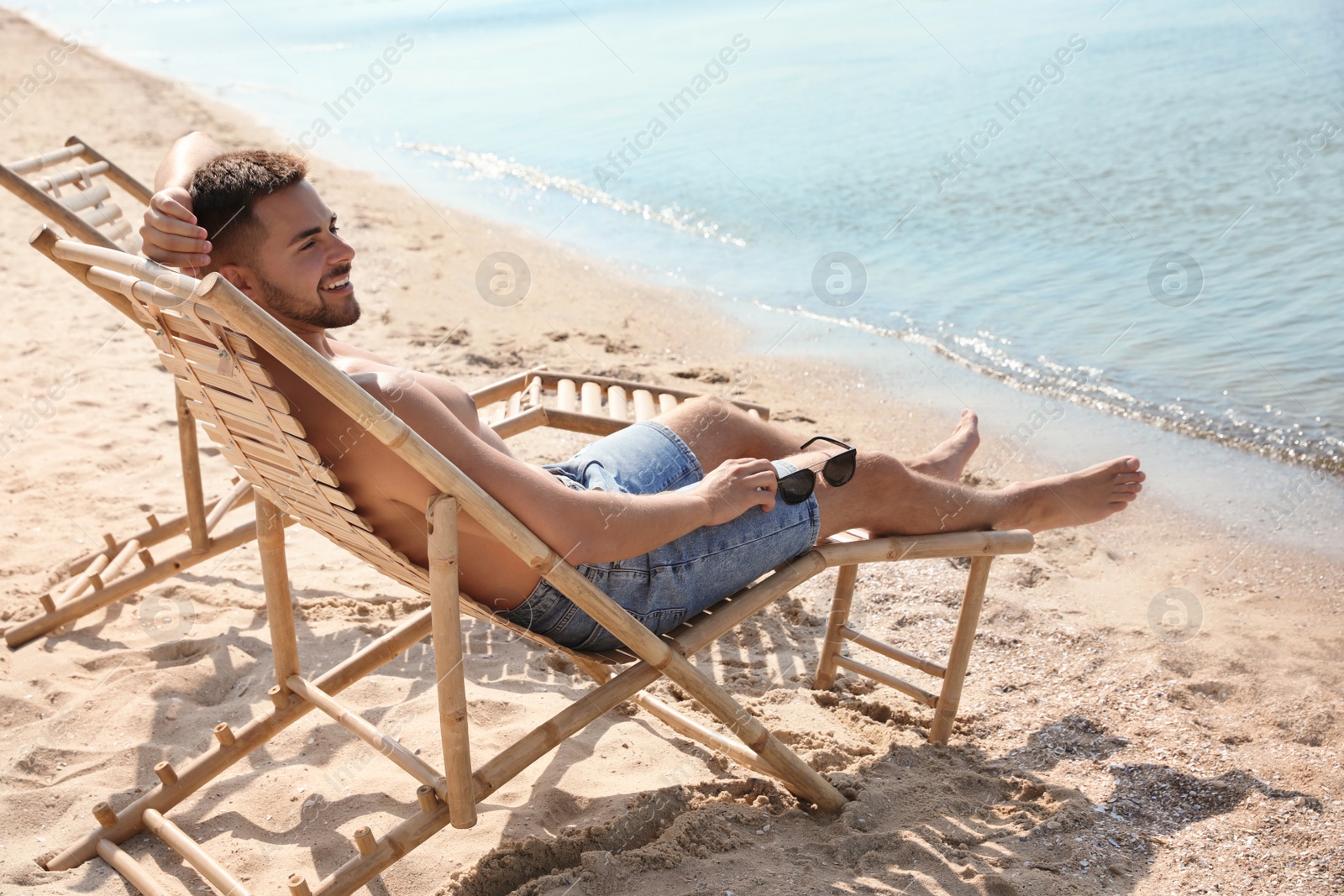 Photo of Young man relaxing in deck chair on sandy beach