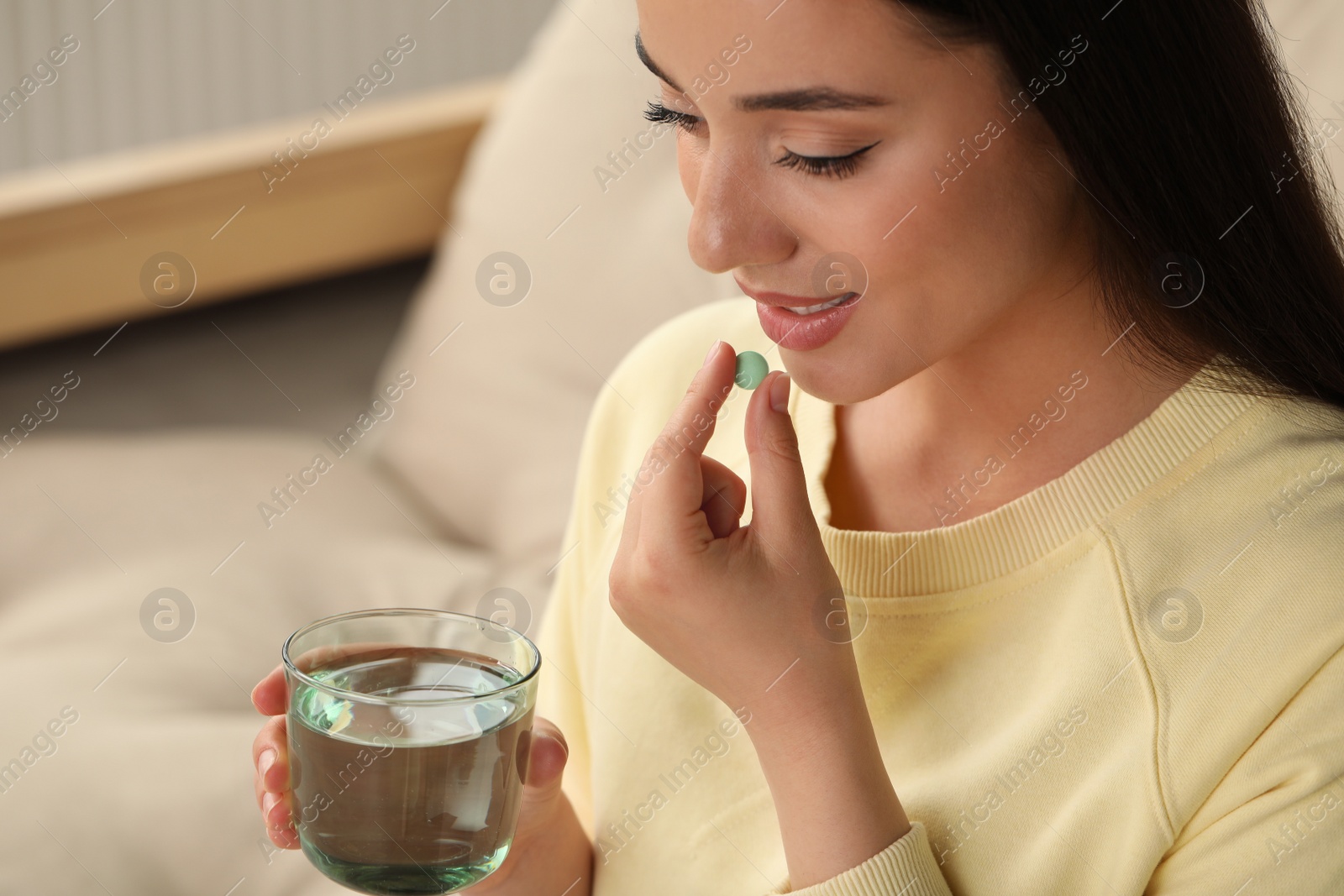 Photo of Young woman with glass of water taking dietary supplement pill indoors, space for text