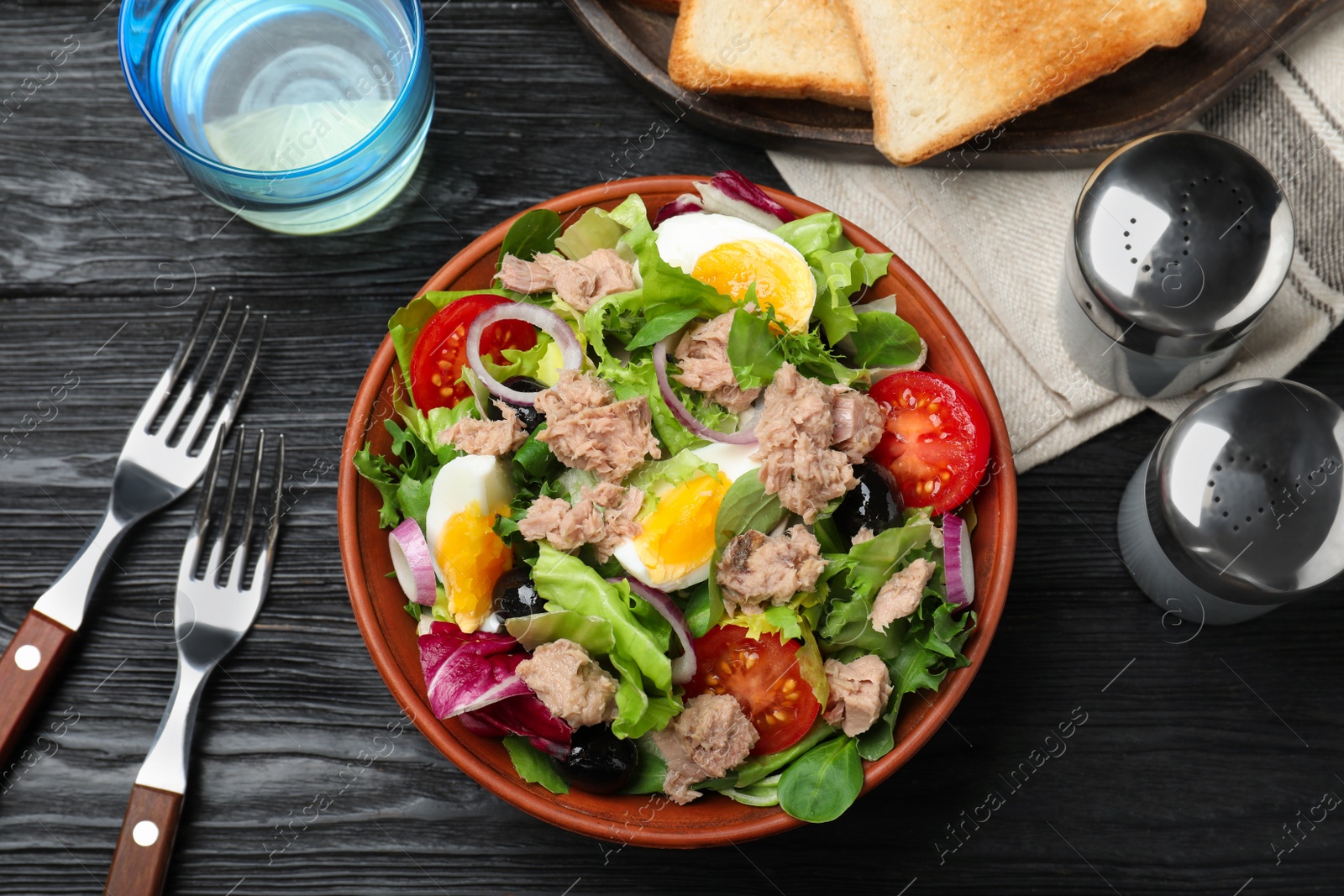 Photo of Bowl of delicious salad with canned tuna and vegetables served on black wooden table, flat lay