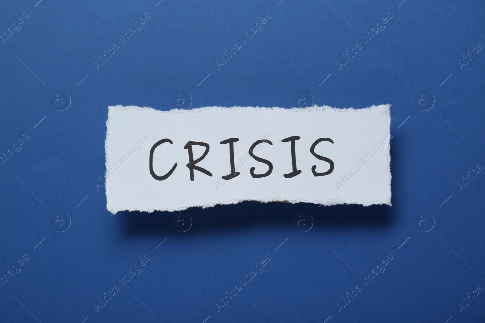 Photo of Paper piece with word Crisis on blue background, top view
