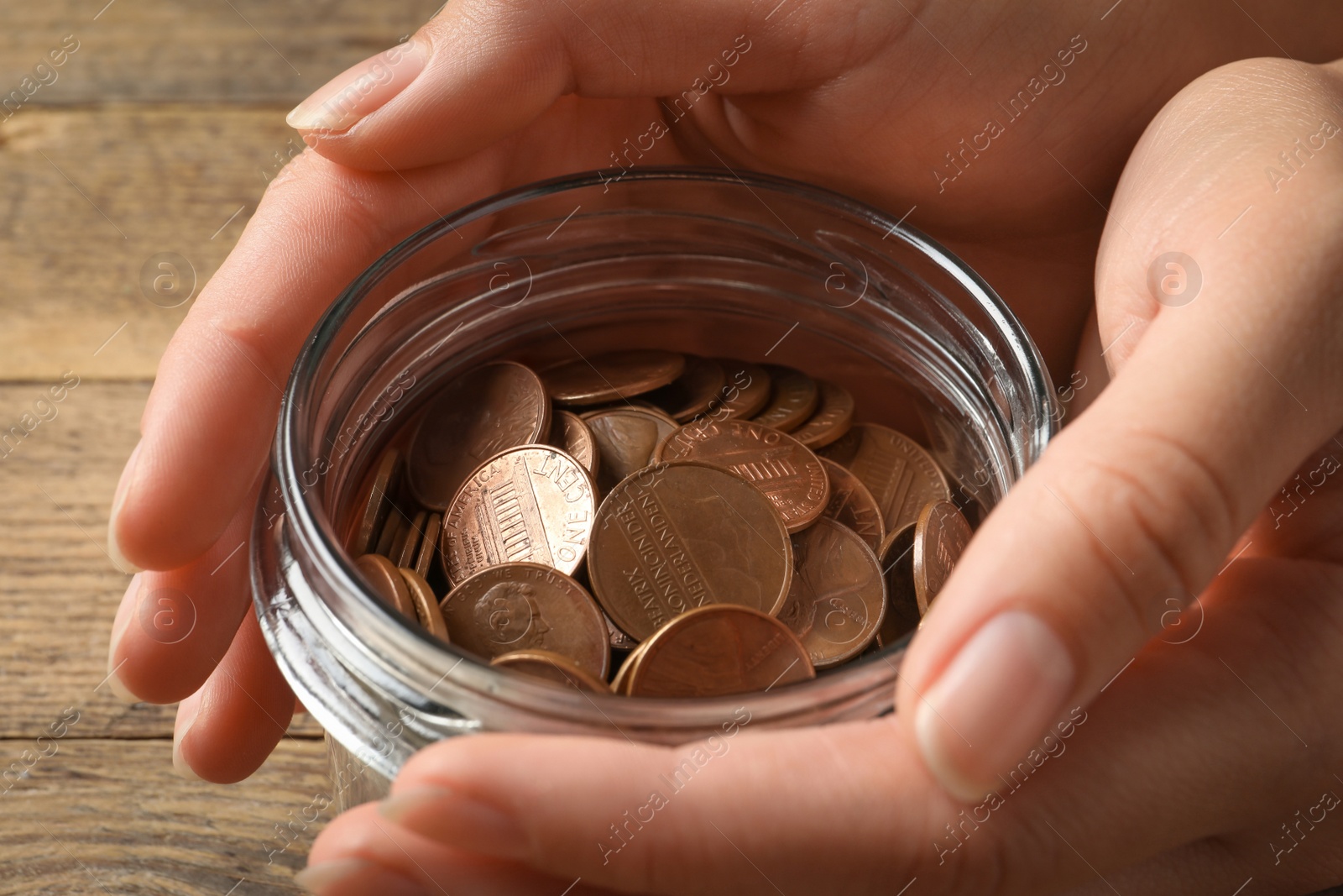 Photo of Woman holding glass jar with coins on wooden table, closeup