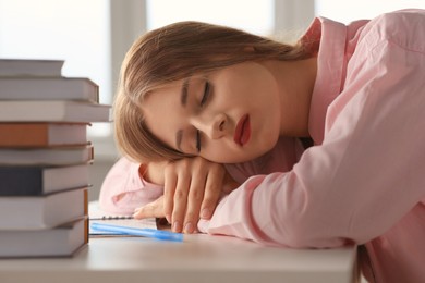 Photo of Young tired woman sleeping near books at white table indoors, closeup