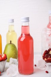 Photo of Tasty kombucha in glass bottles, fresh fruits and ice on white table