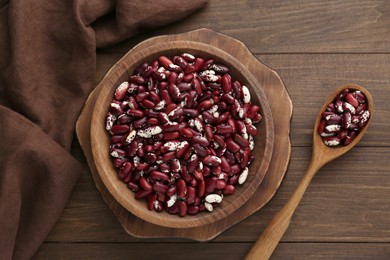 Bowl and spoon with dry kidney beans on wooden table, flat lay