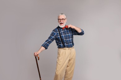 Cheerful senior man with walking cane on gray background