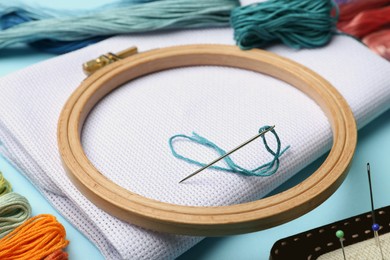 Photo of Embroidery hoop, different threads, fabric and needles on light blue background, closeup