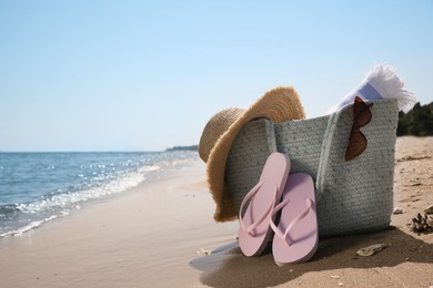 Photo of Bag with beach accessories and flip flops on seaside. Space for text