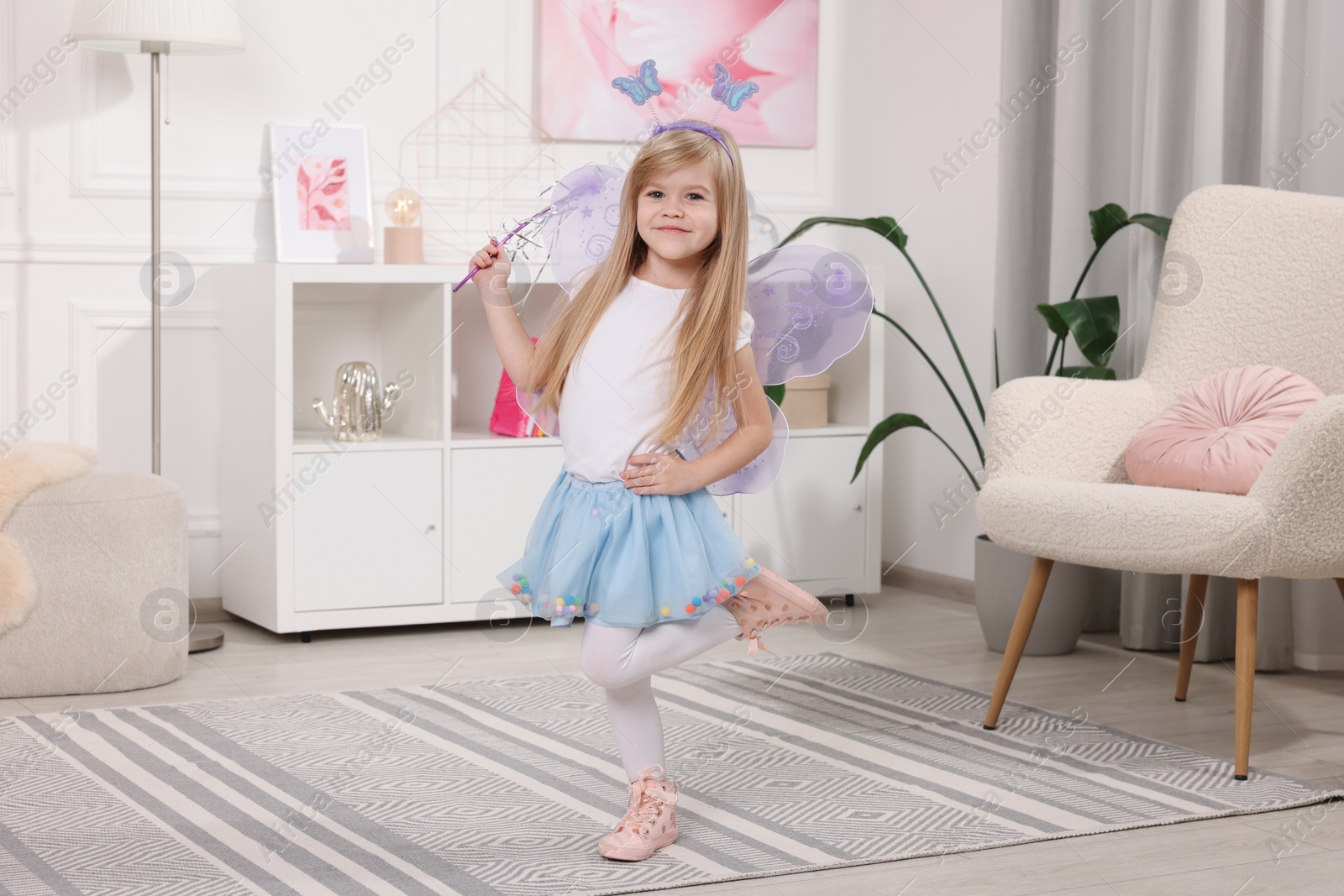 Photo of Cute little girl in fairy costume with violet wings and magic wand at home