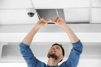 Photo of Technician installing CCTV camera on ceiling indoors