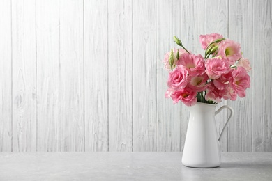 Photo of Eustoma flowers in vase on table near white wall, space for text