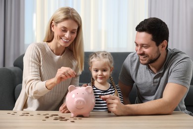 Photo of Family budget. Little girl and her parents putting coins into piggy bank at home