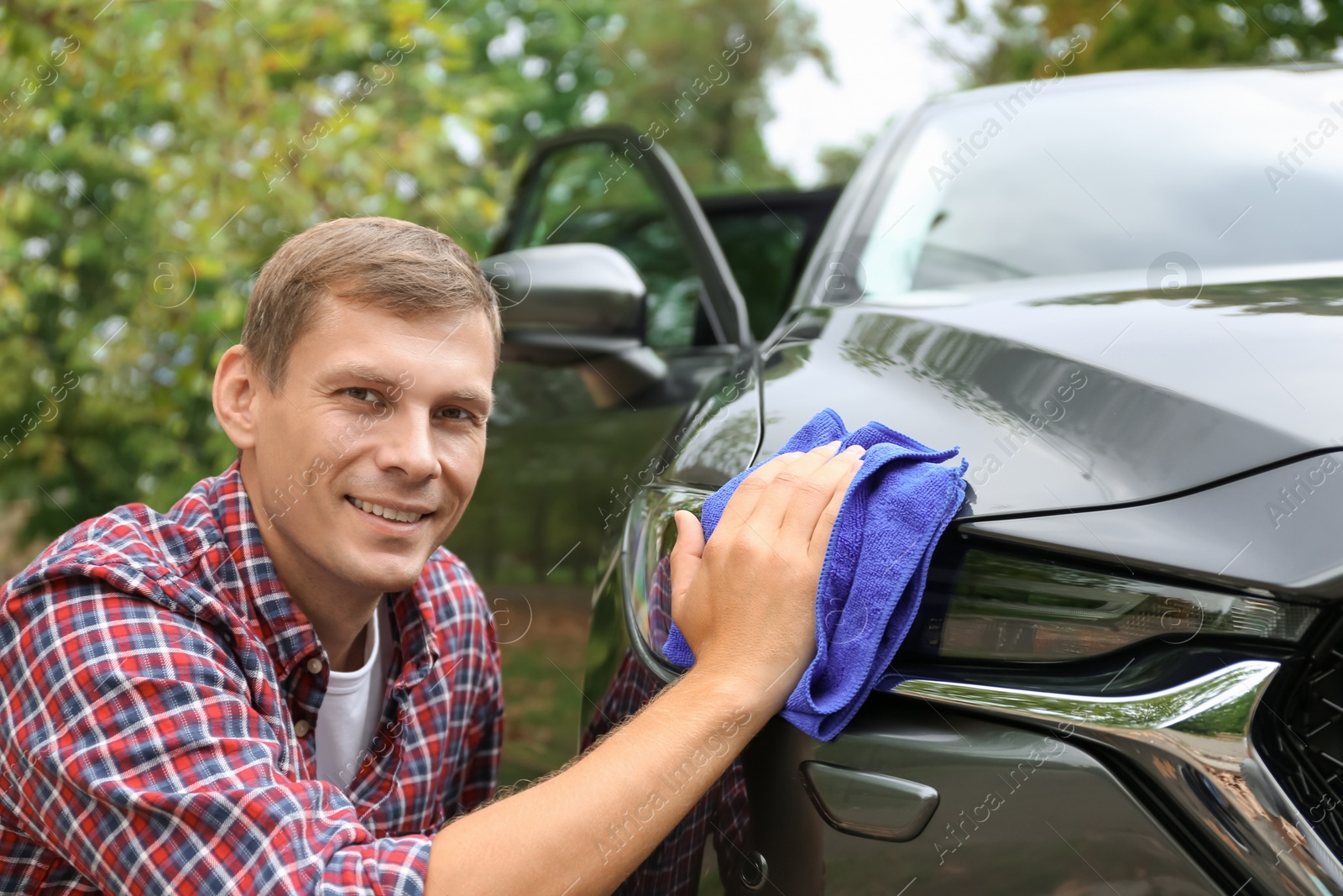 Photo of Man washing car headlight with rag outdoors