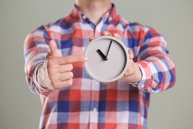 Young man holding alarm clock on grey background. Time concept