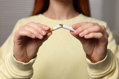 Photo of Stop smoking concept. Woman breaking cigarette on light gray background, closeup