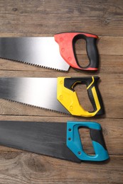 Saws with colorful handles on wooden background, flat lay