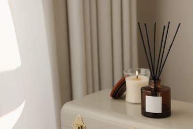 Photo of Aromatic reed air freshener and candle on suitcase indoors, space for text