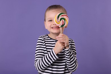 Happy little girl covering eye with colorful lollipop swirl on violet background