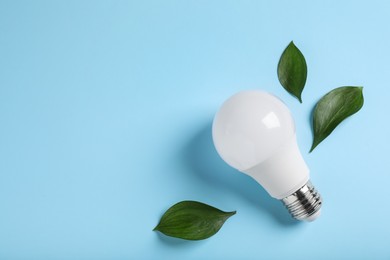 Photo of Light bulb and green leaves on color background, flat lay. Space for text