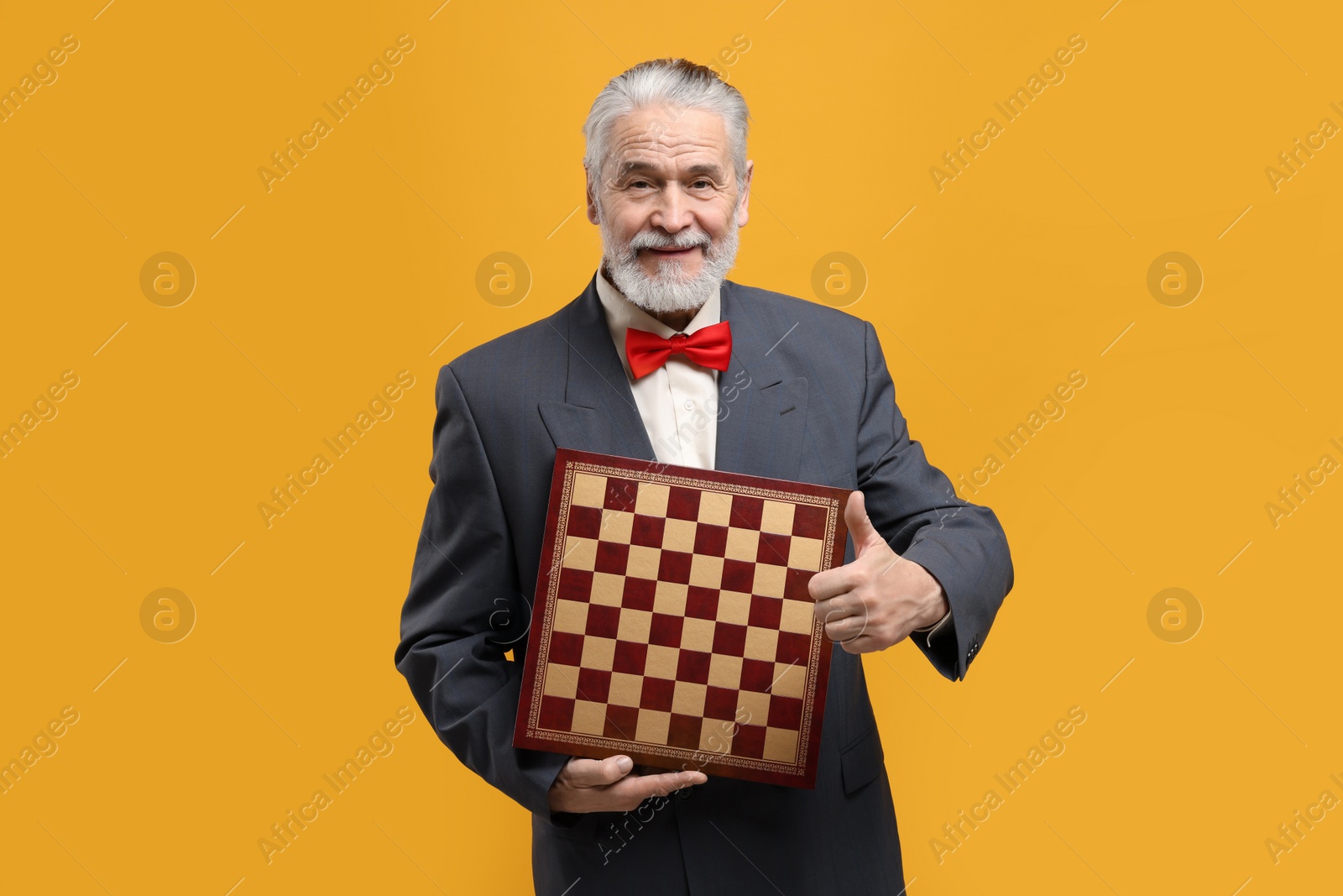 Photo of Man with chessboard showing thumbs up on orange background