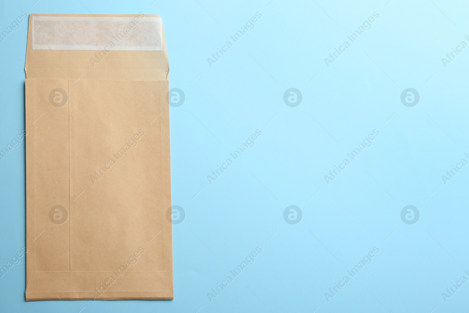 Photo of Kraft paper envelope on light blue background, top view. Space for text