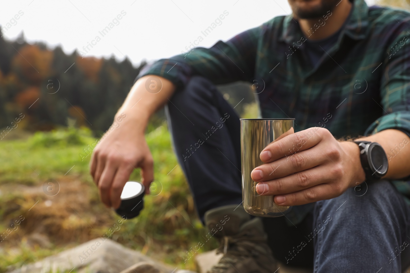 Photo of Man with metallic thermo tumbler in nature, closeup