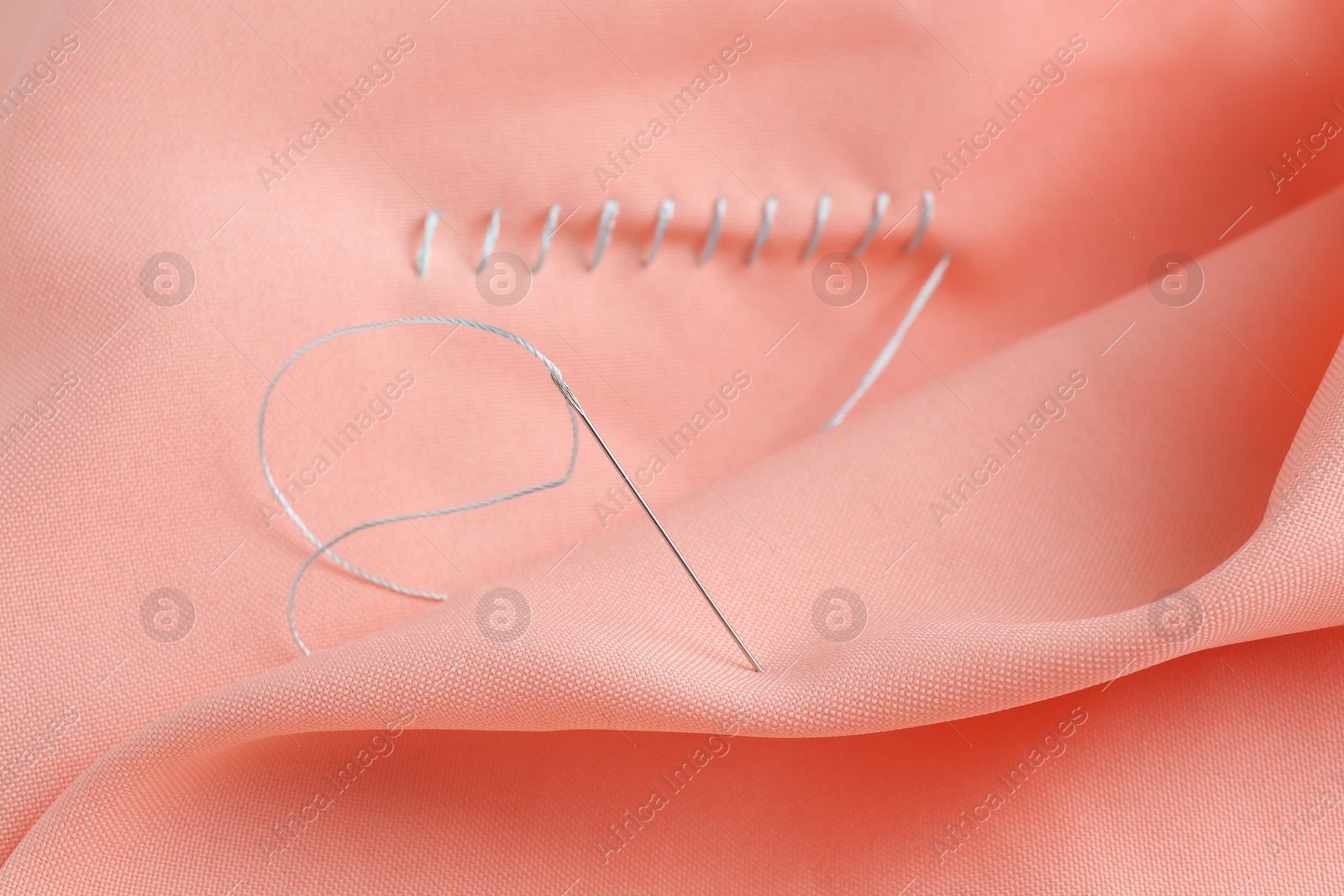 Photo of Sewing needle with thread and stitches on coral cloth, selective focus