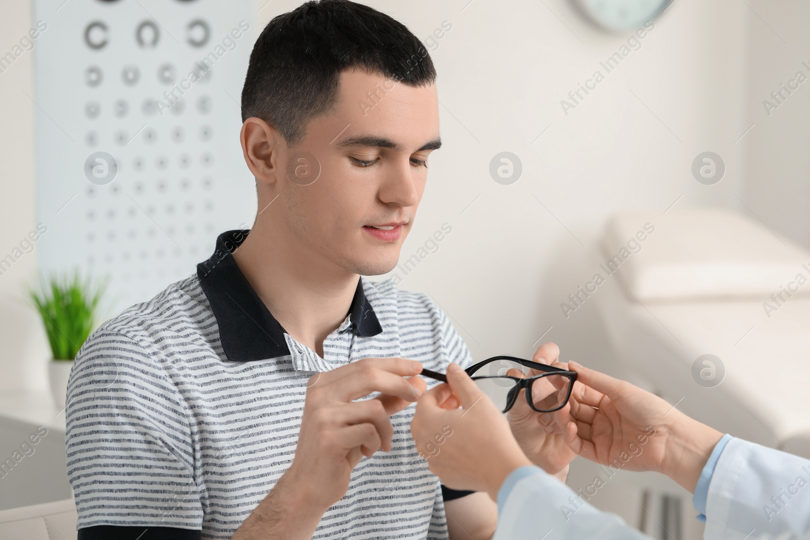 Photo of Vision testing. Ophthalmologist giving glasses to young man indoors