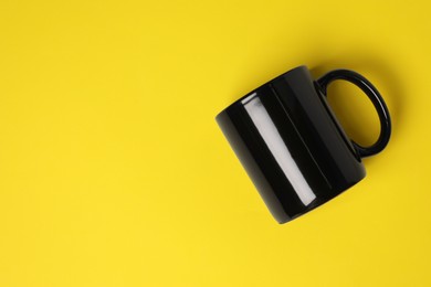 Photo of One black ceramic mug on yellow background, top view. Space for text