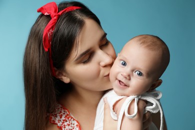 Beautiful mother kissing her cute baby on turquoise background