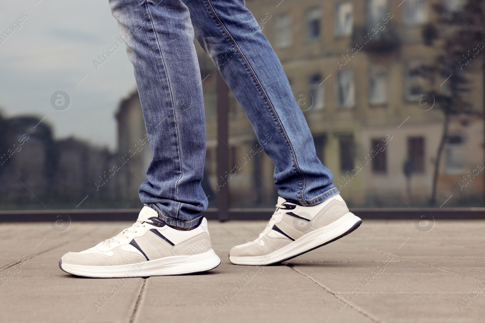 Photo of Man in jeans and sneakers walking on city street, closeup. Space for text