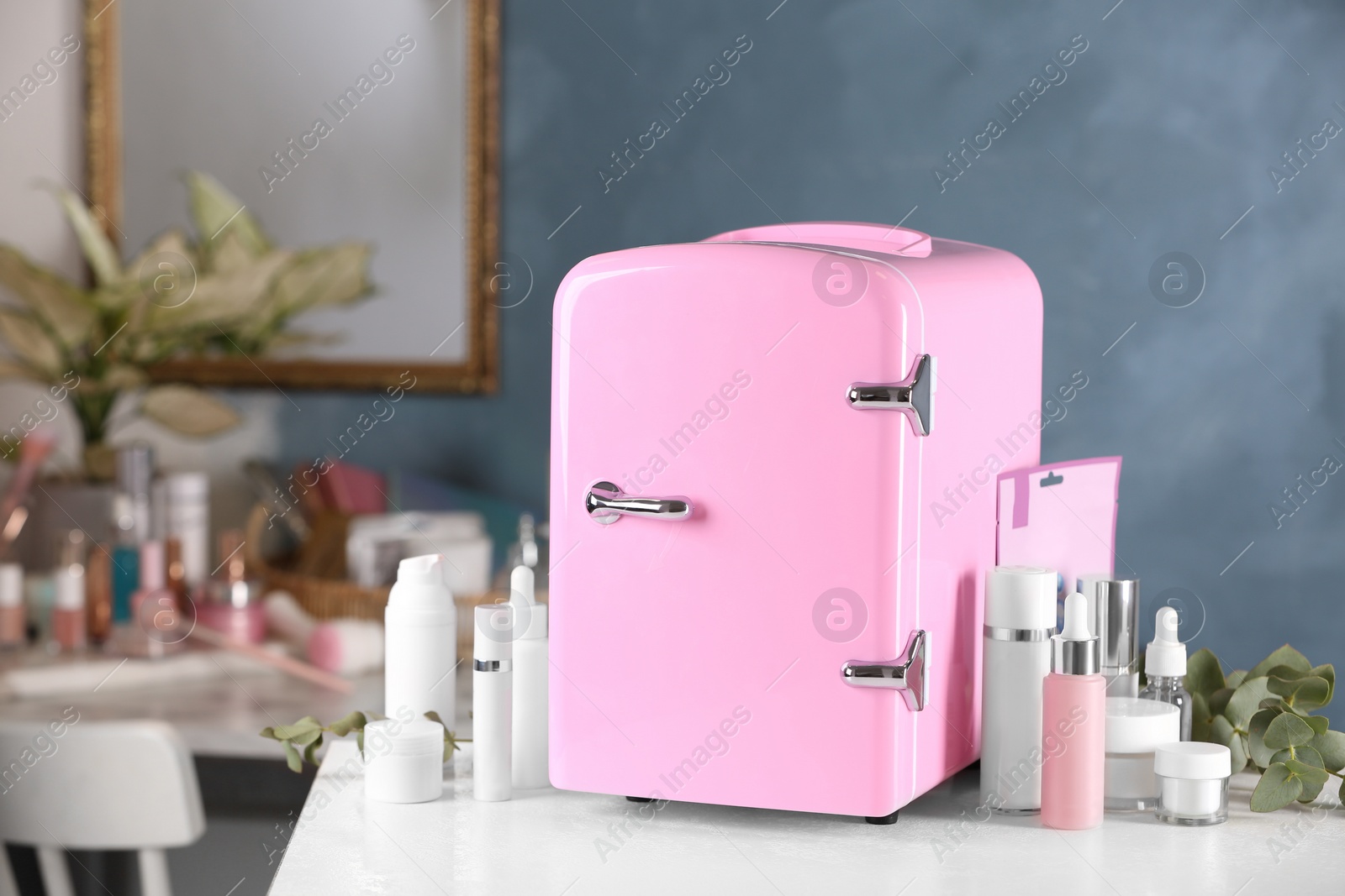 Photo of Pink mini cosmetics refrigerator and skin care products on white table